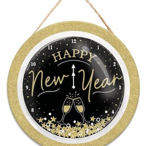 May include: Round wall clock with a gold glitter border and a black face. The clock face reads "Happy New Year" in gold script, with champagne glasses and star accents. A natural twine loop is at the top for hanging.
