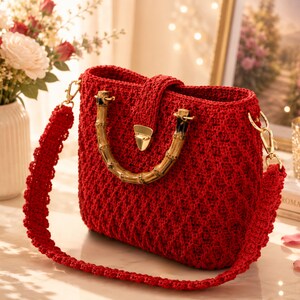 May include: A vibrant red crochet handbag with a bamboo handle and gold-colored hardware. The bag features a detachable shoulder strap and a secure clasp closure. The bag's texture is visible, showcasing the intricate crochet pattern.