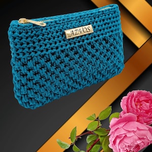 May include: Teal crochet clutch with a gold zipper and a gold metal tag that reads "AZVOS". The clutch is rectangular and has a textured appearance. The background is black and gold with pink roses.