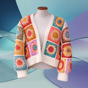 May include: A vibrant, open-front crochet cardigan on a mannequin. The garment showcases a patchwork design with square panels in various colours, including orange, pink, blue, and green, each with a central floral motif. The trim and cuffs are a solid white.