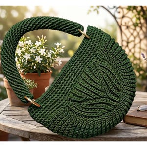 May include: A dark green, semi-circular crochet handbag featuring a thick, rounded handle attached with gold-toned metal rings. The body of the bag displays a textured, leaf-like pattern created through intricate stitching, providing a structured form.