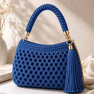 Può includere: Una borsa a mano blu vivace caratterizzata da una trama in macramè testurizzata con un motivo geometrico ripetuto. La borsa include un manico intrecciato abbinato, finiture in metallo dorato e una lunga e spessa nappa blu su una catena dorata.