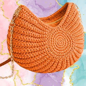 Può includere: Una borsa all'uncinetto arancione con cerniera e catena dorate. La borsa ha un motivo circolare sul davanti e una forma arrotondata. Lo sfondo presenta un design ad acquerello con accenti dorati.