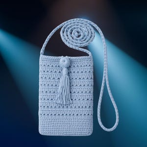 Op de afbeelding: Een lichtblauwe gehaakte crossbodytas met een lange riem. De tas heeft een decoratieve kwast en een textuurpatroon. De riem is een gedraaid koordontwerp. De tas wordt getoond tegen een donkerblauwe achtergrond.