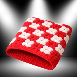 Puede incluir: Un gorro tejido a ganchillo rojo y blanco. El gorro presenta un patrón de tablero de ajedrez de cuadrados rojos y formas de flores blancas con centros amarillos. El borde del gorro es rojo liso.