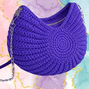 Puede incluir: Un vibrante bolso de mano de ganchillo morado con un diseño en espiral en la parte delantera. El bolso tiene una cremallera plateada y una correa de cadena. El bolso es un accesorio elegante.
