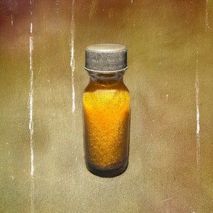 Op de afbeelding: Een klein glazen flesje met een gouden dop en een gouden vloeistof erin. Het flesje staat op een getextureerd, bruin oppervlak.