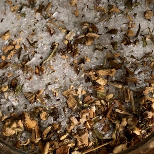 May include: Close-up of a glass jar filled with a mixture of white sugar crystals and dried herbs and roots.