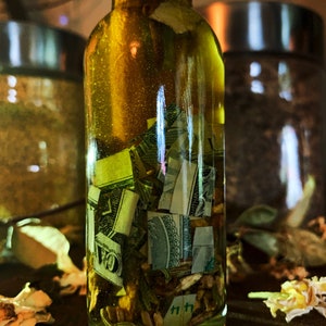 Op de afbeelding: Een doorzichtige glazen fles gevuld met een gele vloeistof en papiergeld. De fles staat op een houten oppervlak.