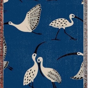 May include: A blue woven throw blanket with a white and black bird pattern. The birds are stylized and have long legs and beaks.