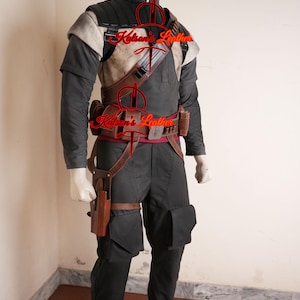 Puede incluir: Un disfraz completo exhibido en un maniquí. El atuendo incluye un chaleco negro y beige, pantalones negros con bolsillos y accesorios de cuero marrón como cinturón, funda y bolsas. El disfraz está diseñado con una estética futurista o militar.