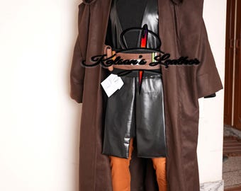 Puede incluir: Un disfraz con capa con capucha marrón, con una parte superior negra, detalles de cuero y pantalones naranjas. El disfraz incluye un cinturón y se exhibe en un maniquí. El tema general es un disfraz de cosplay.