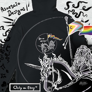 Può includere: Felpa con cappuccio nera con un'illustrazione bianca di una persona che cavalca un unicorno, che tiene una bandiera con un arcobaleno e altri simboli. Il testo "You are safe here" è in un cerchio. Sono visibili anche i testi "Asnescio Designs" e "Only on Etsy".