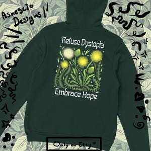 May include: Dark green hoodie with the text "Refuse Dystopia" and "Embrace Hope" above a floral design. The sleeves have decorative black patterns. The brand name "Asnescio Designs" is on the upper left. The Etsy logo is at the bottom.