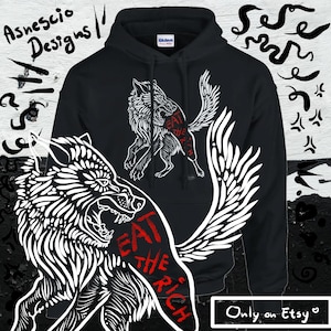 Peut inclure: Sweat-shirt à capuche noir avec un motif de loup blanc et le texte "Eat the Rich" en rouge. Le loup est représenté avec des ailes et une expression de grognement. Le sweat-shirt est disponible sur Etsy.