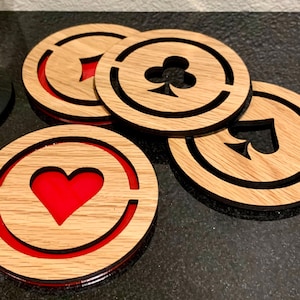 May include: Set of four wooden coasters with playing card suit designs: heart, club, spade, and diamond. Each coaster has a natural wood grain finish with a red accent and a black border. These coasters are perfect for protecting surfaces from drink rings.