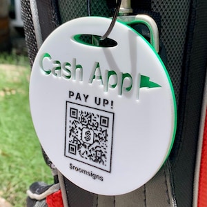 Puede incluir: Una etiqueta redonda blanca y verde con las palabras "Cash App" y "PAY UP!" en verde. También son visibles un código QR y el texto "$roomsigns". La etiqueta está sujeta a un cordón negro y un cierre metálico.