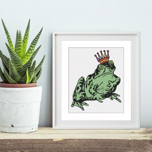 May include: A green frog wearing a colourful crown. The frog is sitting on a white background.