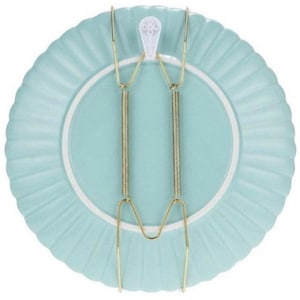 May include: A light blue ceramic plate with a scalloped edge, held by a gold-colored wire plate hanger. The hanger has two vertical springs and a white plastic hook for hanging. The plate is approximately 10 inches in diameter.