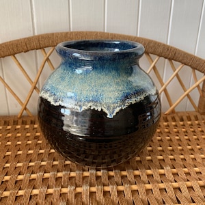 May include: A round, black ceramic vase with a blue and white glaze. The vase has a wide mouth and a narrow base.