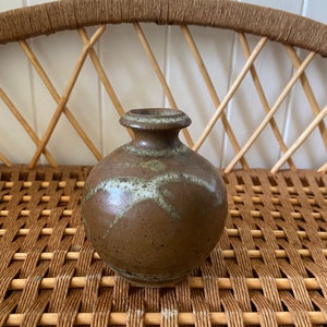 May include: A small, brown ceramic vase with white glaze accents. The vase has a rounded body and a narrow opening.