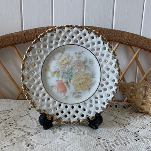 May include: White porcelain plate with a delicate floral design and a gold rim. The plate has a lattice pattern around the edge.