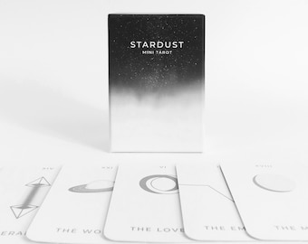 May include: A black box with a white gradient and the text "STARDUST MINI TAROT" on the front. The box is sitting on a white surface with five tarot cards spread out in front of it. The cards are white with black illustrations and roman numerals.