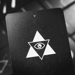May include: Black card with a white triangle containing an eye and the letter "V" in the top right corner.