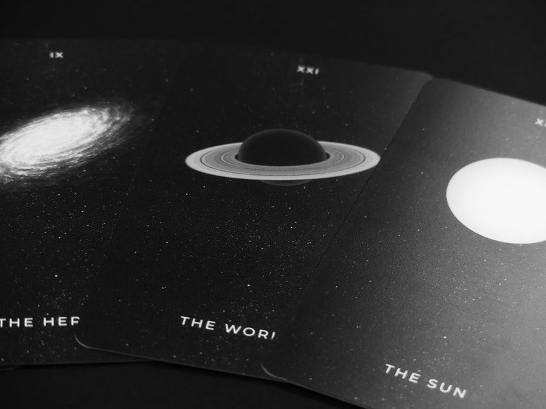 May include: Three black tarot cards with white text and celestial imagery. The first card shows a galaxy, the second card shows a planet with rings, and the third card shows a white circle. The text on the cards reads "The Her", "The Worl", and "The Sun".