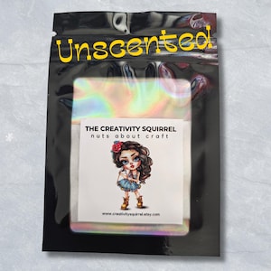 May include: A black, holographic pouch with the yellow text Unscented at the top. A white label in the centre features a cartoon character with brown hair and a blue dress, with the text The Creativity Squirrel nuts about craft.