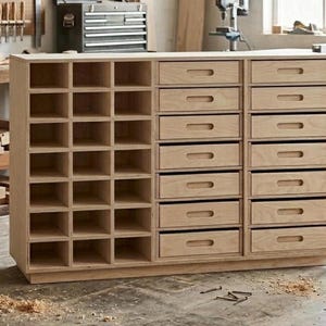 May include: A light-colored wooden cabinet with a combination of cubby shelves and drawers. The cabinet has a rectangular shape and is designed for storage. The drawers have recessed handles, and the shelves are open. The cabinet is made of natural wood.