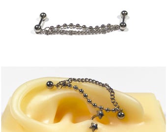 May include: A silver industrial barbell earring with two ball ends connected by a chain of small beads. A second image shows the earring on a yellow ear model, with a star charm.