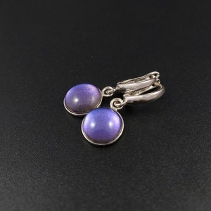 Puede incluir: Un par de pendientes de aro de plata con piedras redondas de color púrpura iridiscente que cuelgan de los aros.