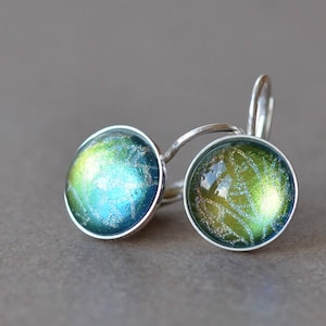 Könnte beinhalten: Ein Paar silberne Ohrringe mit grünen und blauen, irisierenden Glascabochons. Die Cabochons haben eine glitzernde, strukturierte Oberfläche.