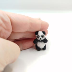 Puede incluir: Un pequeño peluche de panda blanco y negro. El panda está de pie sobre una superficie blanca.