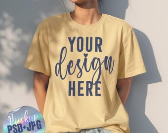 May include: A light yellow t-shirt with the text "YOUR design HERE" in navy blue script. The shirt is a mockup, with a holographic sticker in the lower left corner that says "Mockup PSD+JPG Smart Object Photoshop Drag&Drop in Canva".