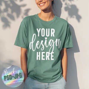 Pode incluir: Uma camiseta verde com o texto "YOUR design HERE" em escrita branca. A camiseta é um mock-up, e a pessoa está usando jeans azuis. Um pequeno adesivo no canto inferior esquerdo diz "Mockup PSD+JPG".