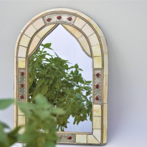 May include: A decorative arched mirror with a white and gold mosaic frame. The frame has red accents and a mirrored surface.