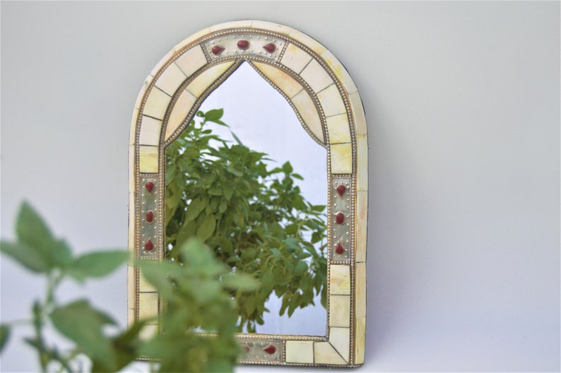 May include: A decorative arched mirror with a white and gold mosaic frame. The frame has red accents and a mirrored surface.