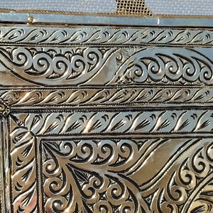 May include: Close-up of a silver metal frame with intricate embossed floral patterns. The frame has a gold border with a decorative design.