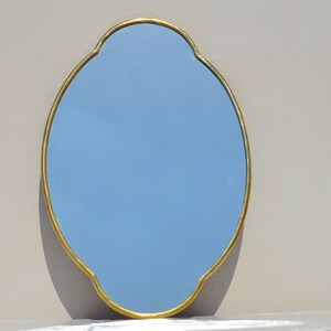 May include: A light blue oval mirror with a gold-colored frame. The frame has a decorative, scalloped edge.