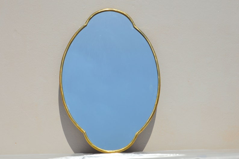 May include: A light blue oval mirror with a gold-colored frame. The frame has a decorative, scalloped edge.