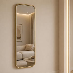 Könnte beinhalten: Ein rechteckiger Spiegel mit goldenem Rahmen hängt an einer beigefarbenen Wand. Der Spiegel spiegelt einen Raum mit einem beigefarbenen Sofa, einem runden Couchtisch und einem gerahmten Kunstwerk wider. Der Spiegelrahmen hat abgerundete Ecken.