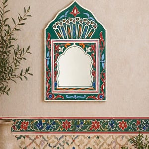 Pu&ograve; includere: Uno specchio da parete decorativo con una cornice dipinta di verde, rosso e bianco. Lo specchio ha una parte superiore ad arco e una forma rettangolare. La cornice presenta intricati disegni floreali e geometrici. Lo specchio &egrave; appeso a una parete beige.