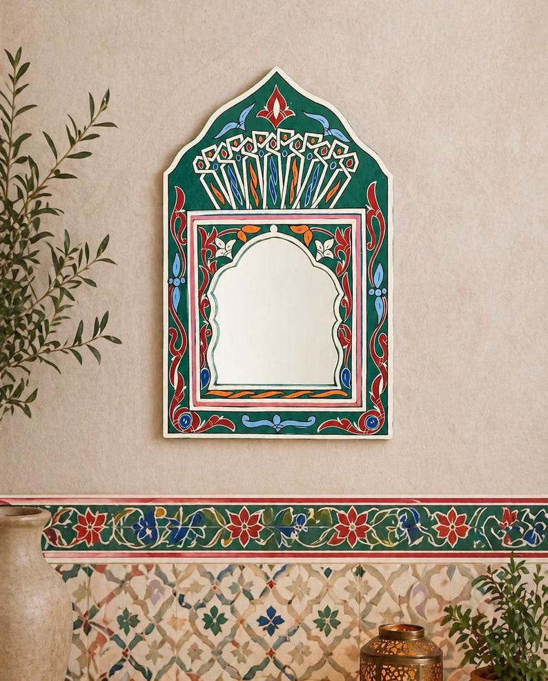 Pu&ograve; includere: Uno specchio da parete decorativo con una cornice dipinta di verde, rosso e bianco. Lo specchio ha una parte superiore ad arco e una forma rettangolare. La cornice presenta intricati disegni floreali e geometrici. Lo specchio &egrave; appeso a una parete beige.