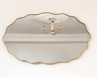 May include: A gold-framed oval mirror with a wavy edge, reflecting a white ceiling with a chandelier.