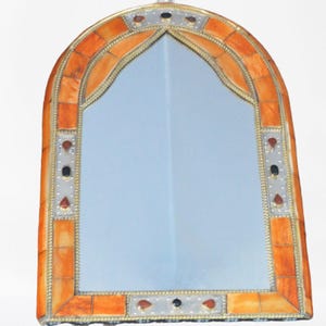May include: A decorative arched mirror with an ornate frame made of inlaid orange and white tiles. The frame is accented with silver metal trim and small, decorative, round, colored stones.
