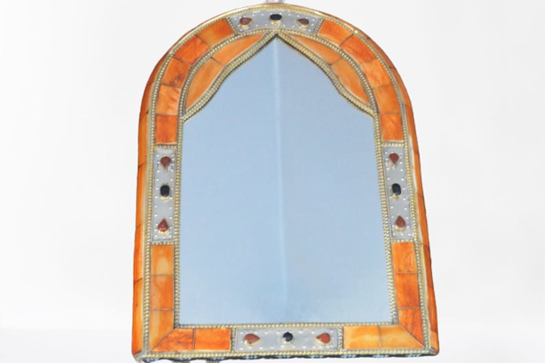 May include: A decorative arched mirror with an ornate frame made of inlaid orange and white tiles. The frame is accented with silver metal trim and small, decorative, round, colored stones.
