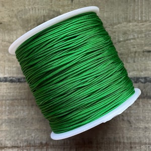 Könnte beinhalten: Eine Spule mit leuchtend grüner Kordel, fest um einen weißen Kunststoffkern gewickelt. Die Kordel hat eine glatte, glänzende Textur. Die Spule liegt auf einer Holzoberfläche.