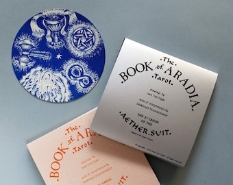 May include: Two book covers for a tarot deck called "The Book of A.Radia Tarot." The covers are pink and silver with orange text. The text on the covers reads "The Book of A.Radia Tarot." and "The 21 Cards of the Aether.Suit."